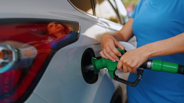 Woman inserts a fuel gun in a gas tank to refuel a car
