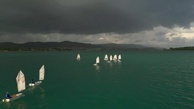 Training sailing yachts class optimist float on the sea.Yachting and sailing training. Summer sport. Aerial view top side of the blue sea and small training sailing yachts with athletes in the regatta
