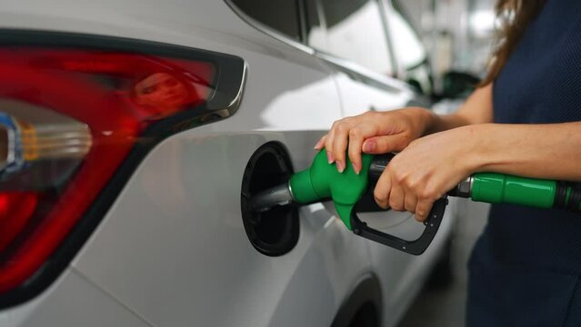 Woman inserts a fuel gun in a gas tank to refuel a car