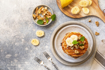 Celebrating Pancake day, american homemade breakfast. Banana gluten free pancakes with nuts and caramel on stone tabletop. View from above. Copy space.