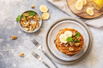 Celebrating Pancake day, american homemade breakfast. Banana gluten free pancakes with nuts and caramel on stone tabletop. View from above.