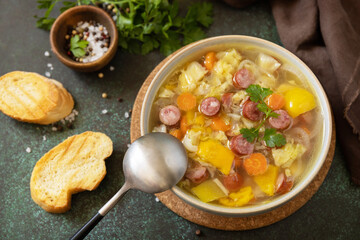 Traditional Zelnacka cabbage soup with sausages and vegetables in a bowl on a stone tabletop. Czech cuisine.
