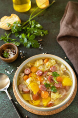 Traditional Zelnacka cabbage soup with sausages and vegetables in a bowl on a stone tabletop. Czech cuisine.