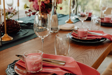 Table setting with cutlery and glass for two persons close-up. On a wooden table are a crystal goblet and a glass next to which are green plates with silver knives and forks