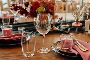 Table setting with cutlery and glass for two persons close-up. On a wooden table are a crystal goblet and a glass next to which are green plates with silver knives and forks