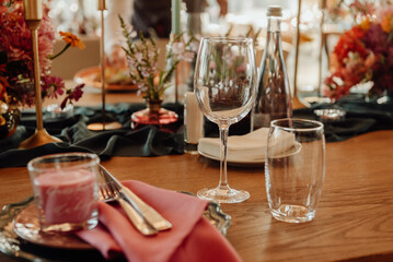Table setting with cutlery and glass for two persons close-up. On a wooden table are a crystal goblet and a glass next to which are green plates with silver knives and forks