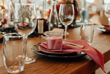 Table setting with cutlery and glass for two persons close-up. On a wooden table are a crystal goblet and a glass next to which are green plates with silver knives and forks