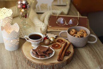 Cup of tea or coffee, various sweets and spices, Christmas decorations, comfy blanket, books and glasses. Selective focus.