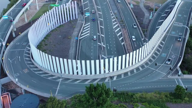 Drone shot of Brisbane ICB motorway junction slowing flying backwards and panning upwards, cars and traffic visible with Brisbane City in background taken at dusk.