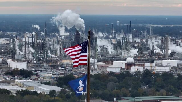 USA and Louisiana flags with oil refinery in distance. Baton Rouge LA long aerial zoom of oil and gas industry theme.