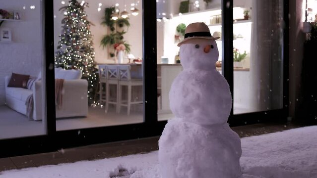 fluffy snow flying on evening patio with snowman and modern aparment during Christmas holidays at the background