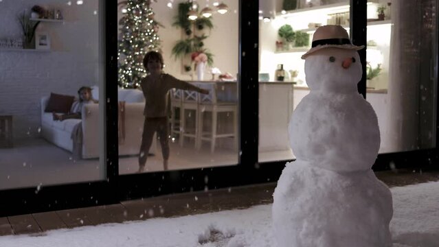 cute kids having fun at home, with snowflakes falling outdoors in winter evening at the background. Cozy, decorated apartment on Christmas holidays