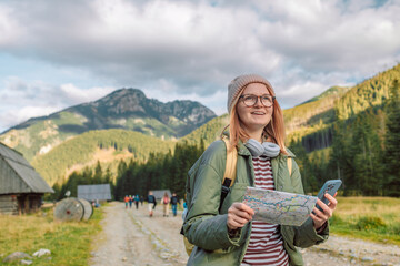 Active young woman holding reading a map while taking a hiking break, having fun and relaxing while spending autumn day outdoors. 