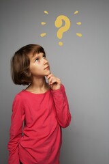 The girl baby is thoughtful, one hand on her chin, looking up, a drawn yellow question mark on a gray background