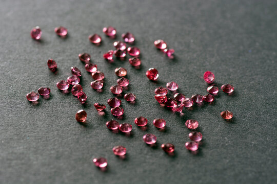 Scattering of natural rich cherry, raspberry rich red round genuine spinel gemstones. Colorful matched small natural unheated spinel gemstone faceted settings. Black paper background. Craft supplies.