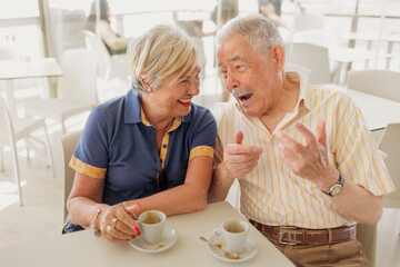 coppia di anziani scherza felice seduti al bar sorseggiando un caffè 