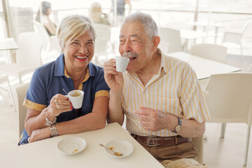coppia di anziani scherza felice seduti al bar sorseggiando un caffè 