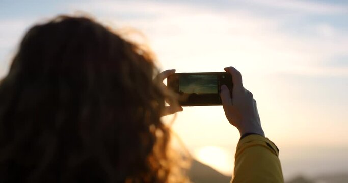 Sunset, phone and woman taking a photo while traveling by by a natural landscape environment. Smartphone, cellphone and female tourist on vacation trip taking a picture at dusk to capture nature