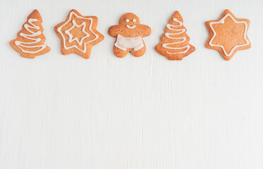 Top view of homemade spiced baked gingerbread cookies or biscuits in shape of man, stars and tree cooked with ginger spice decorated with sweet sugar icing on white wooden background with copy space