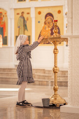a little Christian girl in an Orthodox church puts a candle, prays in front of the icon. High...