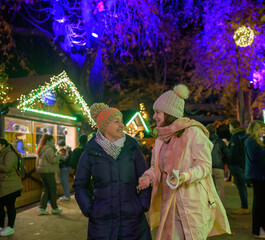 Happy mother and daughter in outerwear walking in Christmas market
