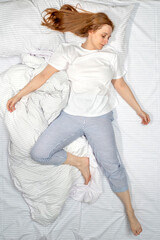 Fototapeta premium Woman sleeping in bed at home. Deep restful sleep. Lady with long brown hair wearing a nightgown. High Angle View girl lying in a nightie on clean white bed linen with cozy blanket