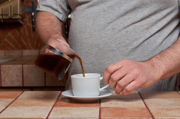 Male hands pour coffee into a coffee cup standing on a tiled kitchen table