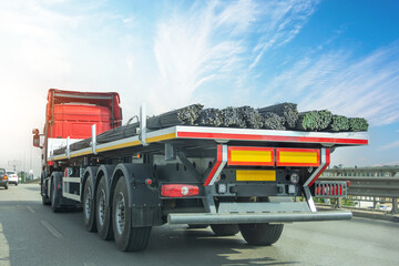 Truck with a long trailer loaded with metal rebar frame for the construction of a building drives along the highway.