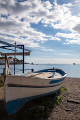 Barca azul y blanca estacionada en la arena de la playa del pueblo catalán de Cadaqués con el mar de fondo bajo un cielo azul con nubes.