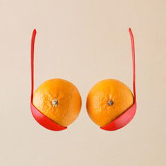 Breast and bra made with oranges or tangerines in bold red ladles on isolated beige background. Minimal aesthetic abstract idea of boobs. Creative food concept with citrus fruit and kitchen equipment.