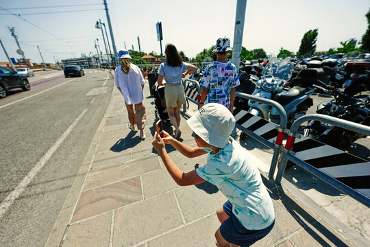Boy tourist making photo on phone walking near mopeds parking on a sunny summer day at Venice, Italy.