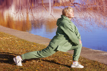 Mature woman in a green fleece hoodie doing stretching in the autumn park.