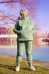 Mature woman in a green fleece hoodie doing stretching in the autumn park.