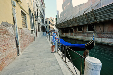 Fototapeta na wymiar Boy stand near canal with covered gondola in Venice, Italy.