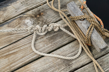 wooden jetty with boat mooring point and ropes attached displaying knots.