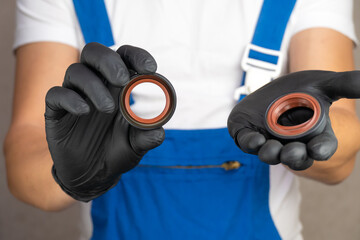Auto mechanic in blue jumpsuit holds engine oil seal in black gloves. Car engine and oil leak...