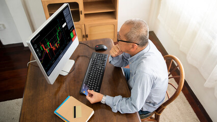 Senior asian man using computer trading stock market exchange online at home.