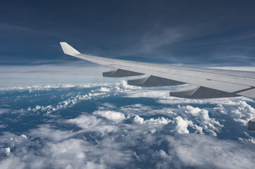 Obraz premium Wing of airplane above flat fluffy clouds surface with soft evening sunlight. Copy space.