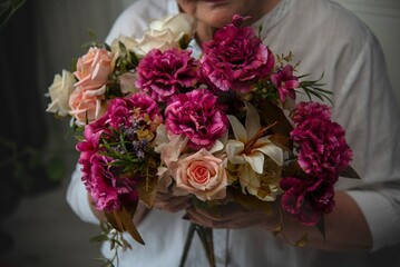 A bouquet of white roses and burgundy carnations in the hand of a woman in a white shirt