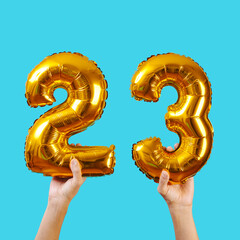 holds two balloons forming the number 23