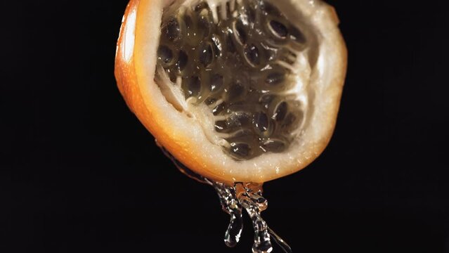 Slow Motion Macro Shot of Flowing Granadilla Juice from Halved Granadilla in black Background