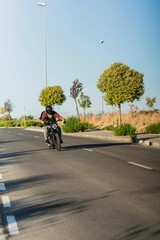 Tattooed man with a helmet riding his bike on the asphalt road on a sunny day