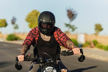 Tattooed man with a helmet riding his bike on the asphalt road on a sunny day