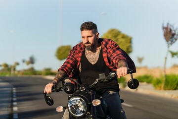 Tattooed man riding his bike on the asphalt road on a sunny day