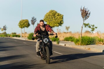 Tattooed man riding his bike on the asphalt road on a sunny day