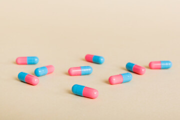 Heap of pink and blue pills on colored background. Tablets scattered on a table. Pile of red soft gelatin capsule. Vitamins and dietary supplements concept