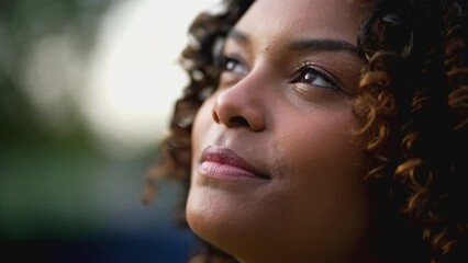 Hopeful young black woman opening eyes to sky smiling. Grateful happy African American latina 20s girl. Faithful contemplative emotion