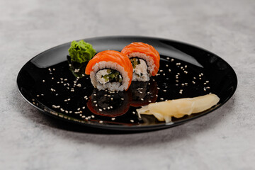 Two portions of sushi with salmon and cucumber with vossabi sauce and ginger on a black plate. Side view
