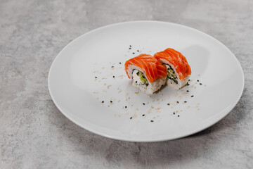 Two portions of sushi with salmon and cucumber on a white plate.