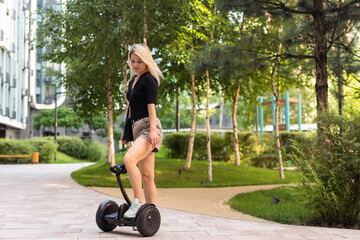 woman riding electric mini segway hover board scooter in green park. Good summer weather,...